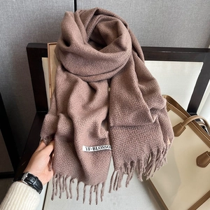 Detailed view of brown houndstooth knitted scarf with fringe and brand label