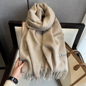 Close-up of beige knitted scarf with fringe details and woven brand label