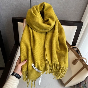 Detail of yellow houndstooth knit scarf featuring elegant fringes and a woven side label