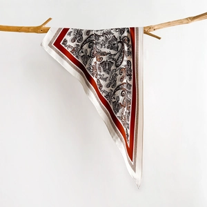 Detail of paisley print silk scarf with satin finish hanging on a natural wooden branch
