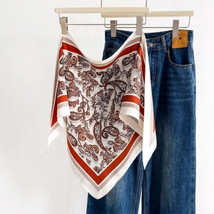 Ivory paisley pattern silk scarf with red border hanging on a white clothes hanger