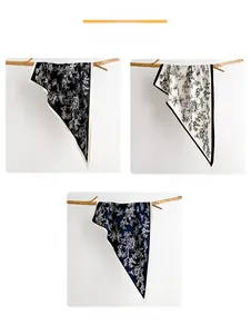 Floral print silk scarves in black, white, and navy blue displayed on a wooden branch
