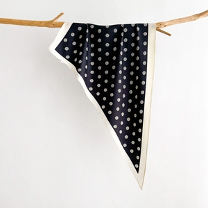 Navy polka dot silk scarf with cream borders draped over a natural wooden branch