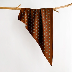 Detail of silk scarf with green polka dots on brown fabric draped over a wood branch