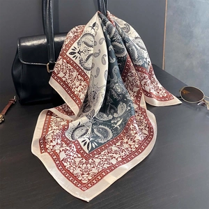 Dettaglio di un foulard in seta di gelso con motivo paisley drappeggiato su una borsa in pelle