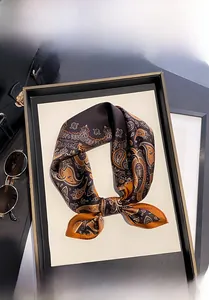 Detail of paisley 100% mulberry silk scarf displayed with luxury accessories on a tray