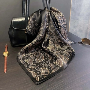 Elegant black and gold silk scarf with paisley patterns draped on a handbag