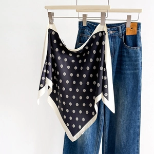 Polka dot silk scarf with black and white print hanging on a hanger with jeans