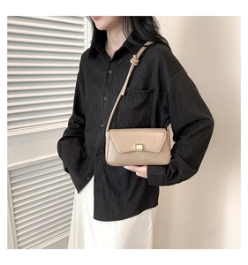 Dettaglio borsa baguette beige goffrata coccodrillo con fibbia dorata su camicia nera