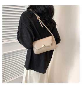 Dettaglio di borsa a spalla beige effetto coccodrillo con chiusura in metallo dorato su modella