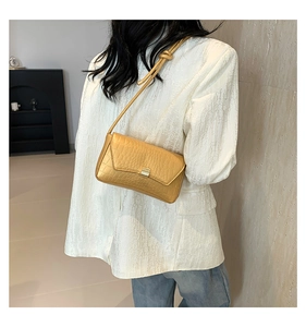 Dettaglio di una borsa a tracolla dorata con stampa coccodrillo su blazer bianco
