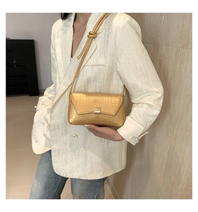Dettaglio borsa baguette dorata con trama a coccodrillo e fibbia metallica su blazer bianco