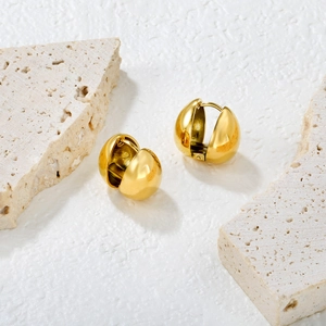 Polished chunky gold hoop earrings with water drop heart shape on white stone background