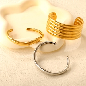 Detail of 18K gold and silver plated crossover open bracelets on a decorative tray