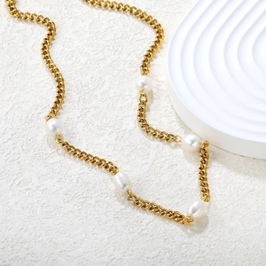 Macro detail of golden 18K plated chain and baroque freshwater pearls on a textured background