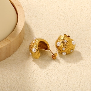 Détail de boucles d'oreilles C dorées avec texture martelée et perles blanches chic