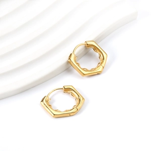 Détail macro de boucles d'oreilles hexagonales dorées avec texture ondulée sur plateau