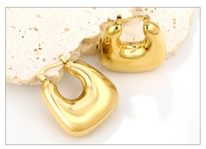 Gros plan de boucles d'oreilles dorées géométriques avec finition miroir sur pierre brute