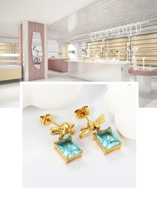 Detail of gold knot earrings featuring a light blue rectangular crystal drop charm