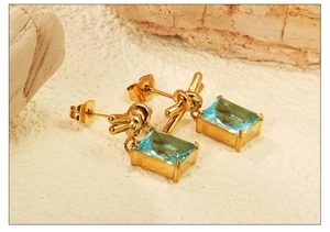 Macro shot of gold knot earrings featuring a rectangle light blue gemstone and stud back
