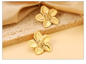 Macro detail of gold flower earrings with ribbed petals on stone and satin background