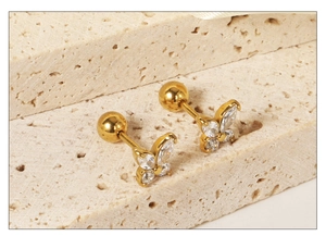 Gros plan de boucles d'oreilles papillon dorées avec zircons blancs sur pierre beige