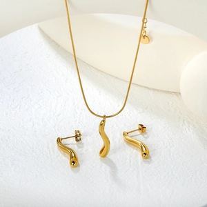 Minimalist gold wave pendant necklace and stud earrings set on a white textured background