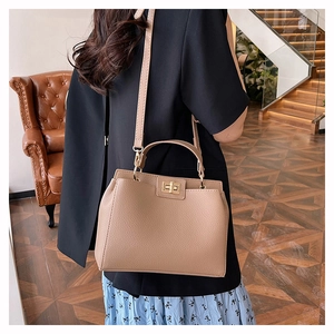 Sac à bandoulière en cuir beige avec boucle dorée porté à l'épaule par un mannequin
