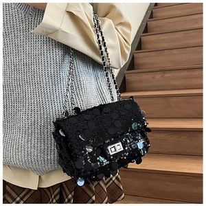 Detail of a black sequin chain crossbody bag worn by a model on a wooden staircase