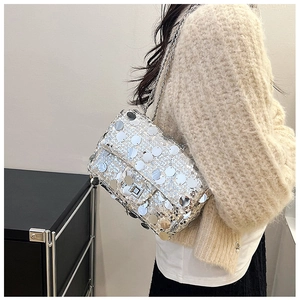 Detail of silver sequin crossbody bag showing metal chain and twist lock on knit sweater
