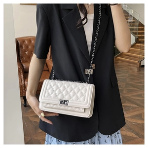 White quilted crossbody bag with silver chain strap and twist lock on a black blazer