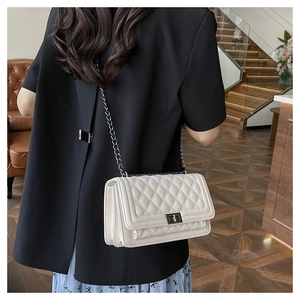 White quilted crossbody bag with black metal chain strap and turn-lock on a model