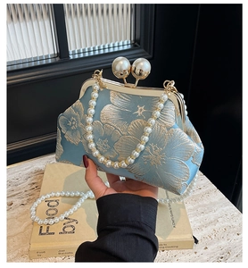 Detailed embroidery of gold floral patterns on light blue fabric with pearl bag clasp