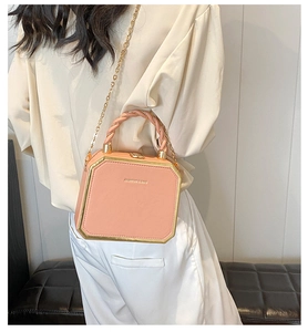 Model showing a pink box bag with gold metal frame and twisted handle on a black bench
