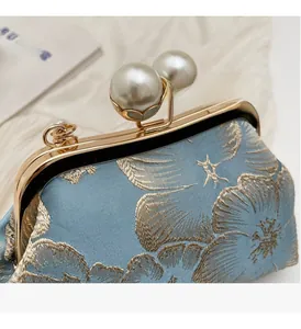 Detailed view of floral embroidery on light blue satin with gold pearl clasp closure