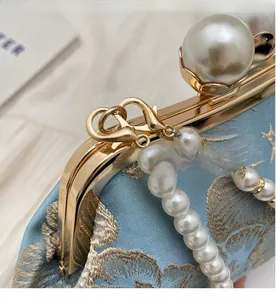 Close-up of golden metal frame with large pearl clasp and luxury embroidery on light blue bag