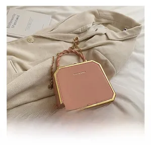 Detail of pink octagonal crossbody bag with gold frame and twisted handle on beige fabric