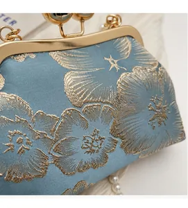 Macro shot of gold floral embroidery and pearl chain detail on light blue satin handbag