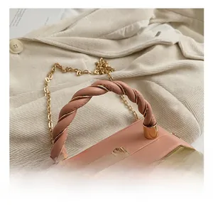 Detail of twisted pink leather and gold metal handle on a structured crossbody bag