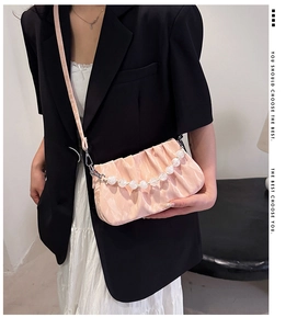 Detail van roze geplooide cloud bag met elegante acryl parel handvat op een model