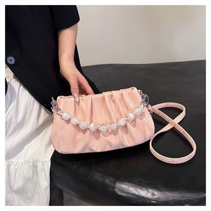 Detail van roze geplooide crossbodytas met witte kralenketting en fijne stofstructuur