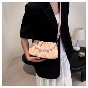 Detail van beige geplooide handtas met elegante parelgreep en slanke verstelbare riem