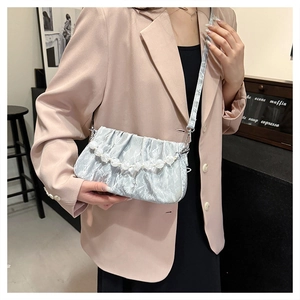 Detail van lichtblauwe geplooide cloud bag met parelketting en zijdeachtige textuur