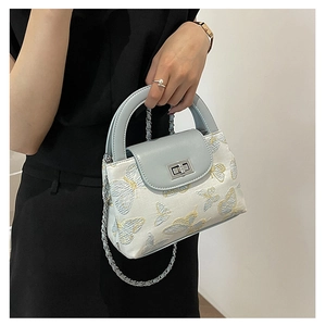 Close-up of light blue quilted bucket bag with elegant butterfly embroidery and silver clasp