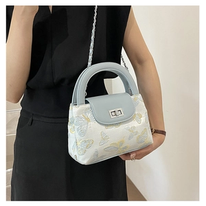 Detail of light blue bucket bag featuring butterfly embroidery and metal chain strap