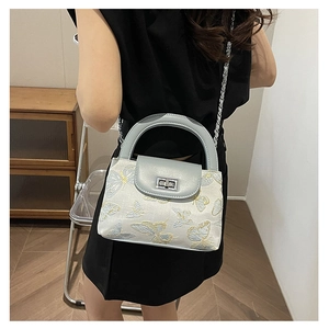 Detail of light blue quilted bucket bag with butterfly embroidery and silver chain strap