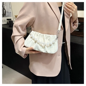 Detail van een witte gerimpelde handtas met parelketting gedragen bij een beige blazer
