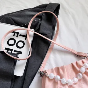 Detail van roze geplooide handtas met marmeren kralen op een grijze blazer achter