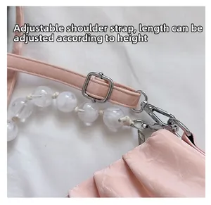 Detail van verstelbare leren riem en acryl parelketting op roze schoudertas