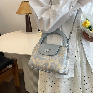 Light blue quilted bucket bag with gold abstract print and silver chain strap crossbody